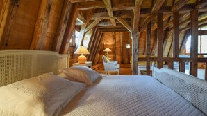 Ein gemütliches Schlafzimmer im Dachgeschoss mit einem großen Bett, Holzbalken und einem kleinen Tisch mit einer Lampe.