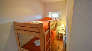 A small, single-bedded room with a wooden bunk bed, a bedside table with a lamp, and a window providing natural light.