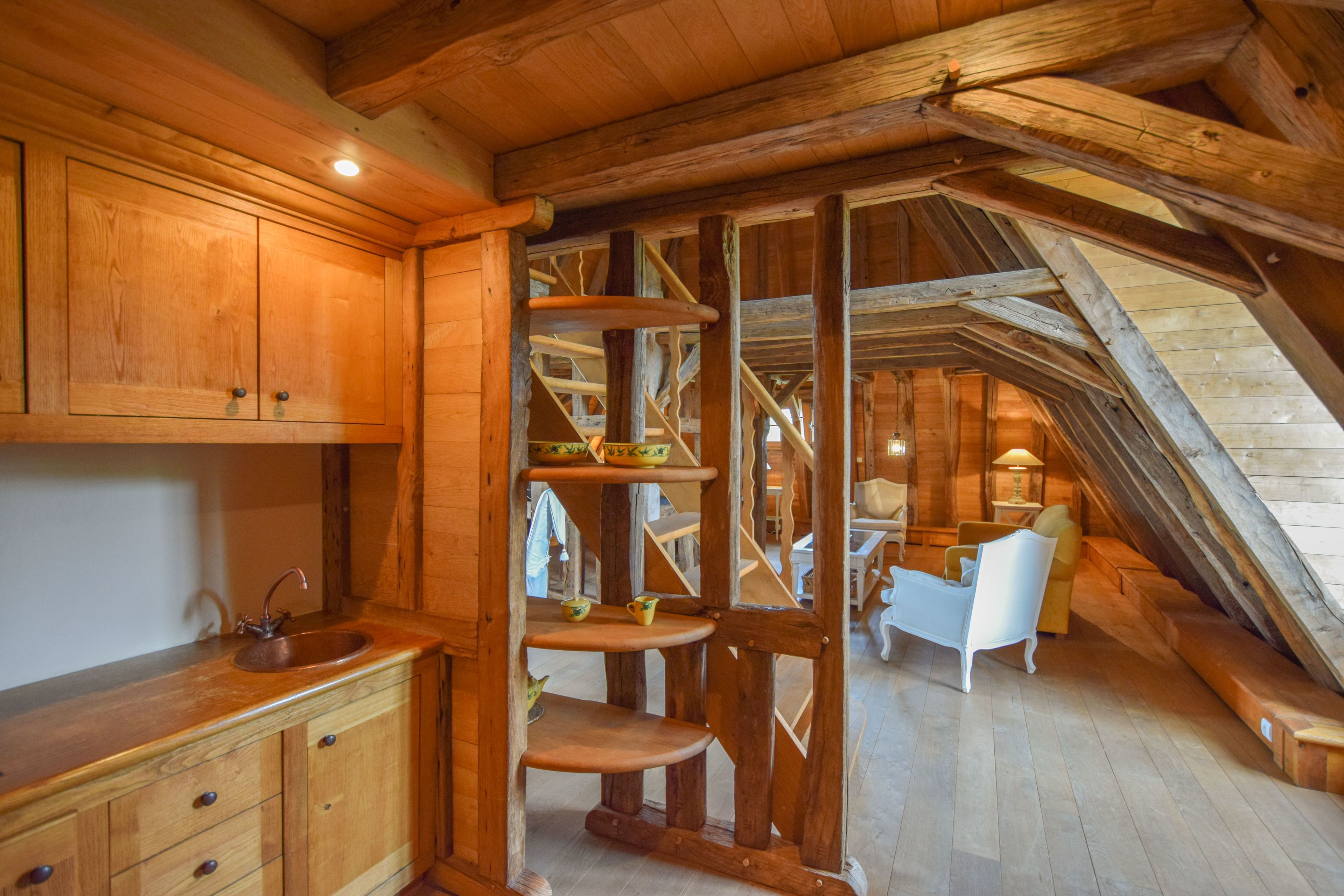 A rustic wooden interior with a kitchen area, a staircase, and a seating area.