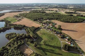 Vue aérienne d’une zone rurale avec des champs, un lac et un ensemble de maisons dotées de piscines.