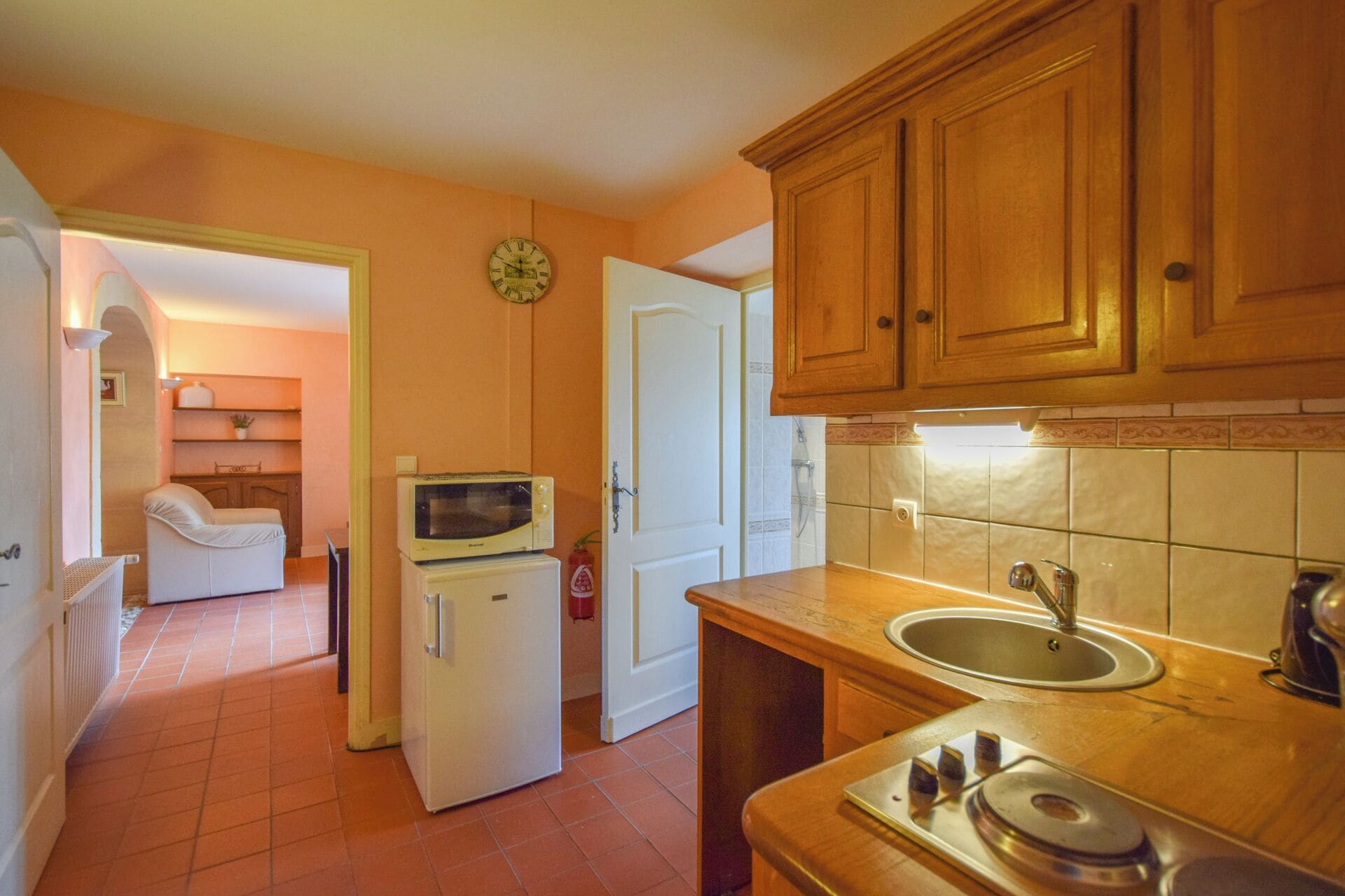 A compact kitchen with wooden cabinets, a microwave on top of a refrigerator, a sink, and a stove.