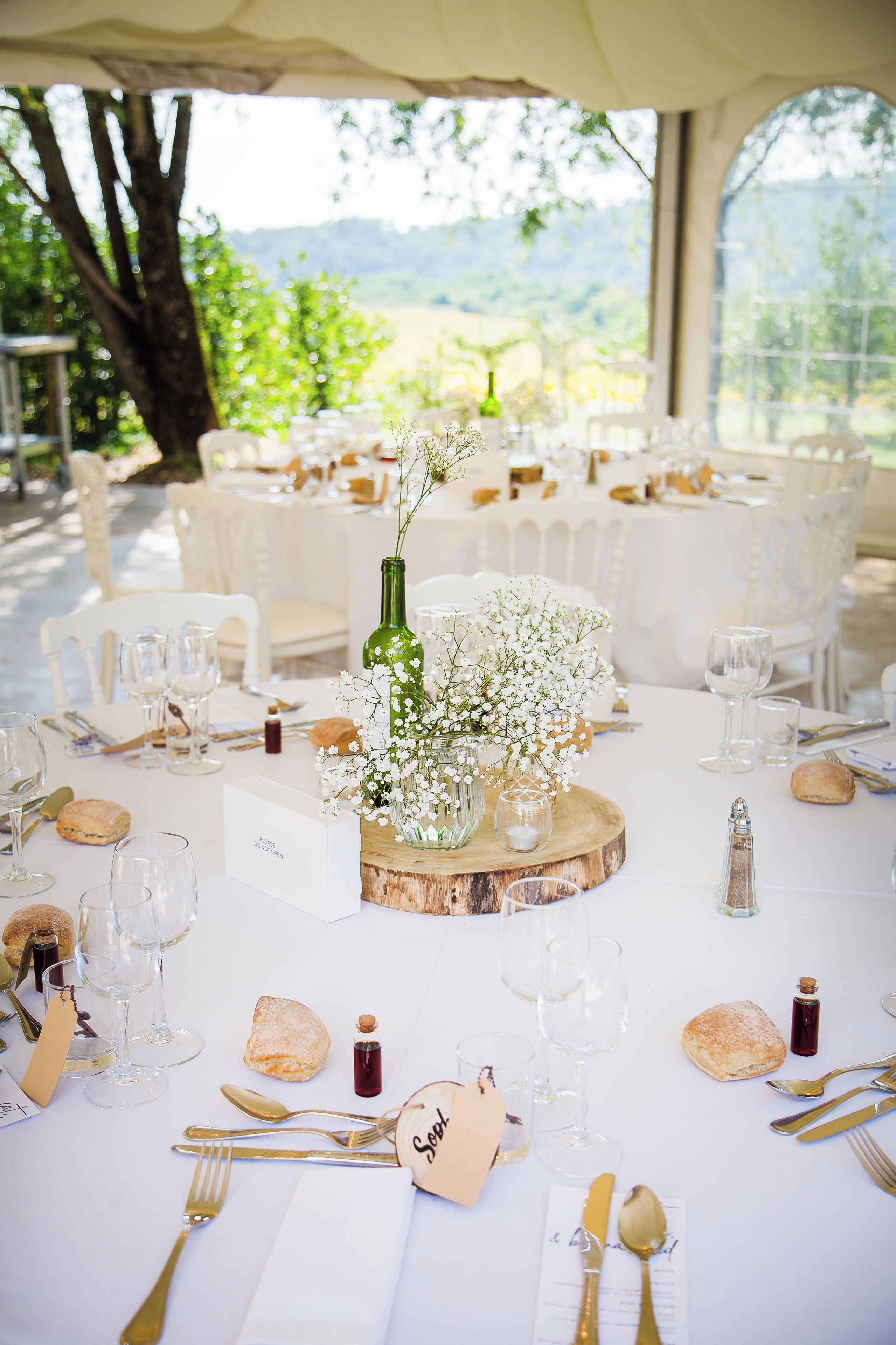 Mesa dispuesta para una recepción de bodas, con manteles blancos, cristalería y un centro de mesa con flores y una botella verde.