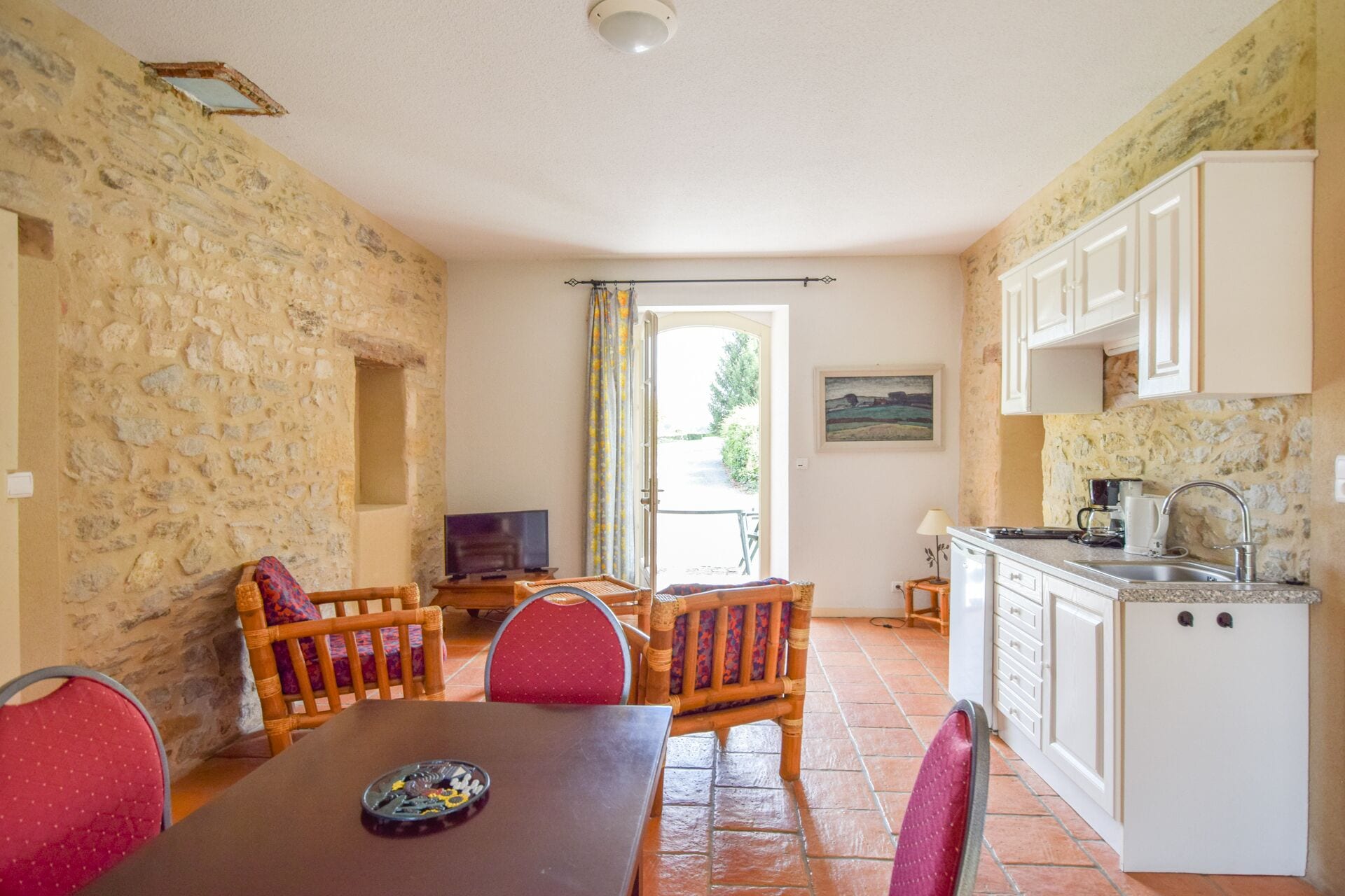 Una habitación acogedora con pared de piedra, una mesa de comedor con sillas, televisión y una zona de cocina con armarios y un lavabo.
