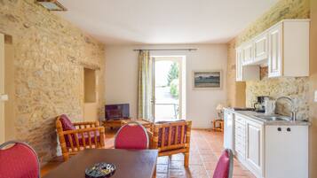 Una habitación acogedora con pared de piedra, una mesa de comedor con sillas, televisión y una zona de cocina con armarios y un lavabo.