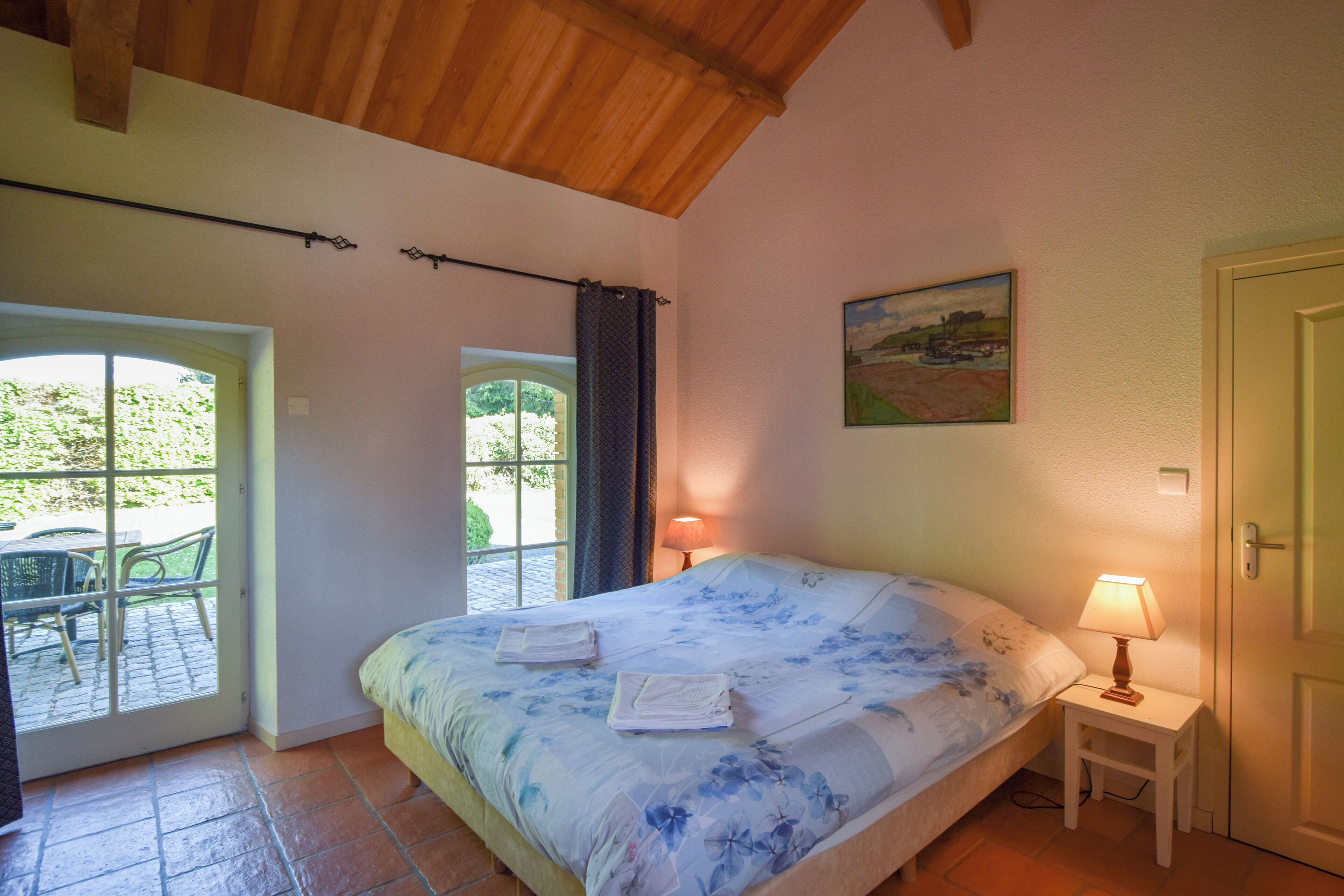 Un dormitorio con cama, una mesita de noche con lámpara, una puerta y una ventana con cortinas.