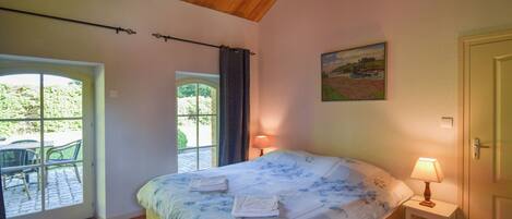 Un dormitorio con cama, una mesita de noche con lámpara, una puerta y una ventana con cortinas.
