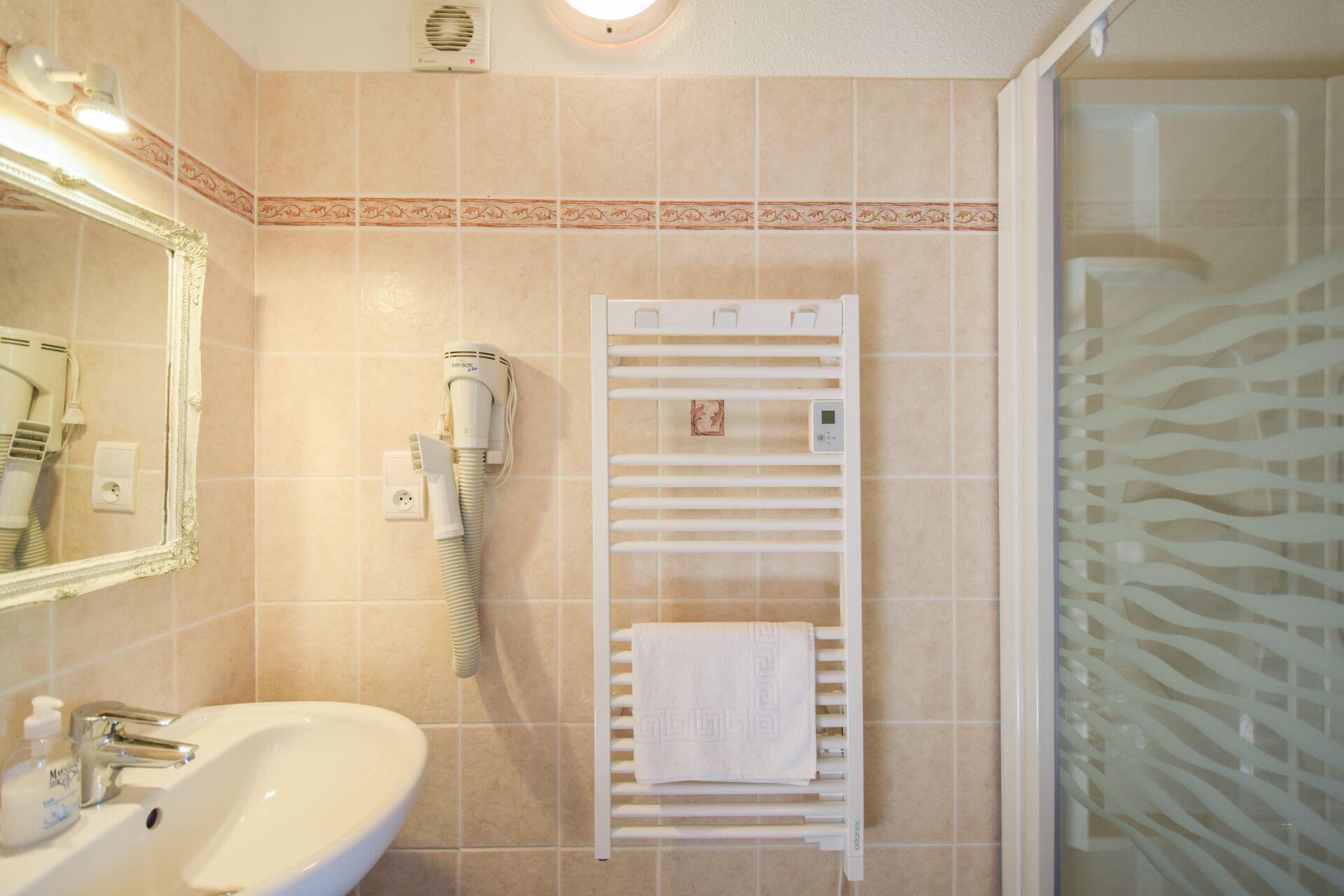 Une salle de bain équipée d’un lavabo, d’un miroir, d’un sèche-cheveux, d’un porte-serviettes et d’une douche.