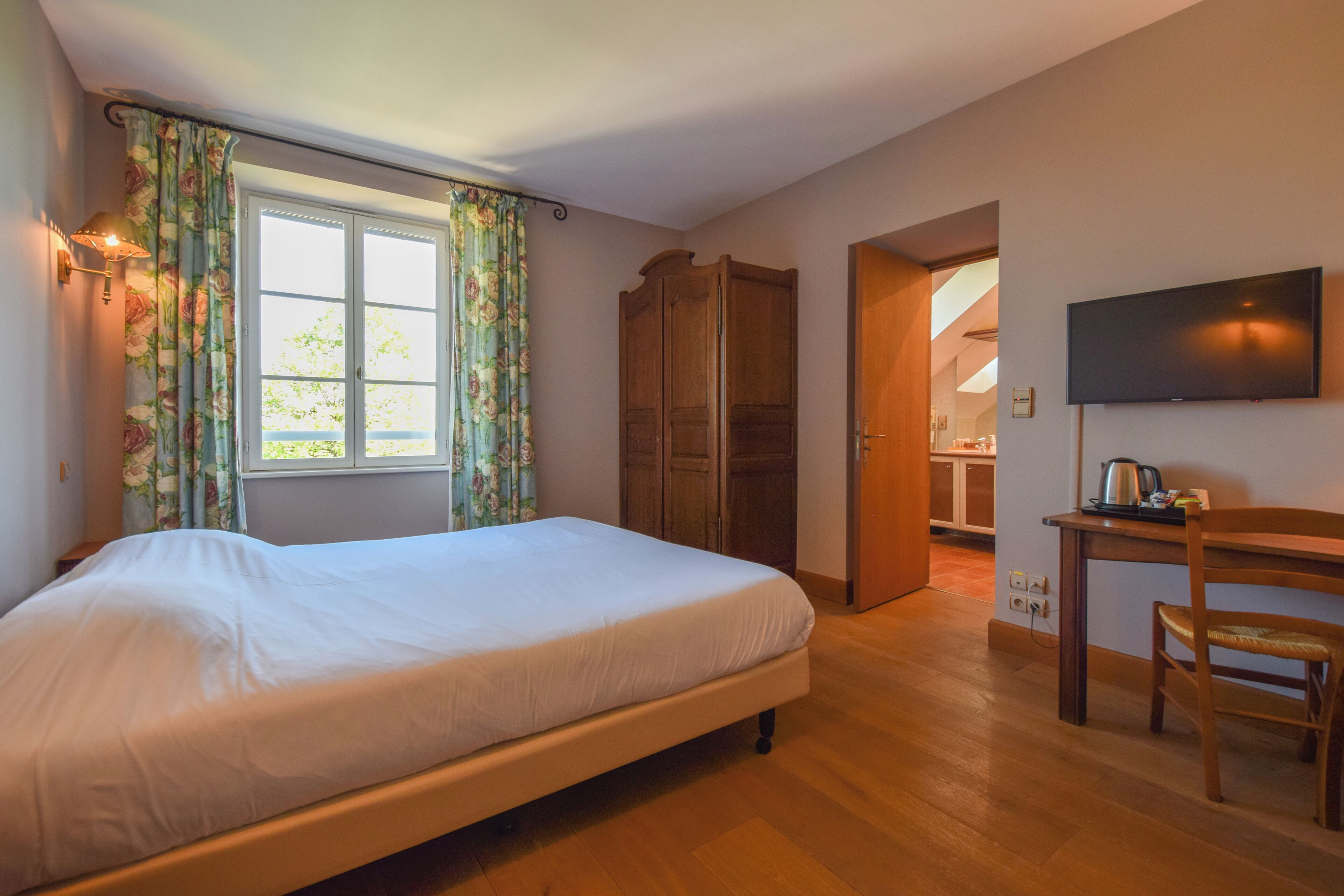 A bedroom with a bed, a wooden wardrobe, a television, and a desk with a chair.