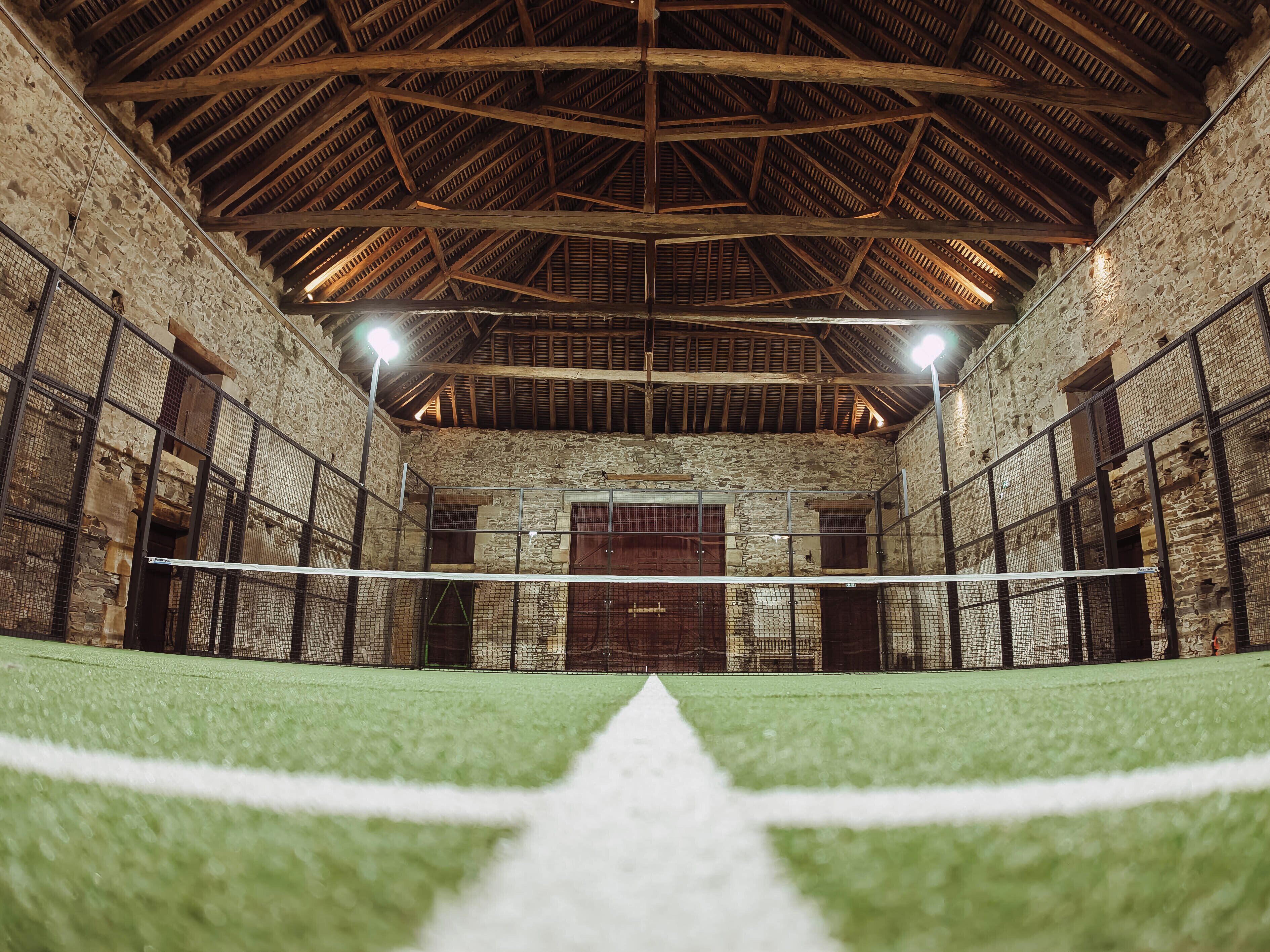 An indoor sports facility with a netted volleyball court, stone walls, and wooden beams.