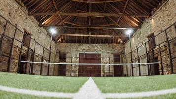 An indoor sports facility with a netted volleyball court, stone walls, and wooden beams.