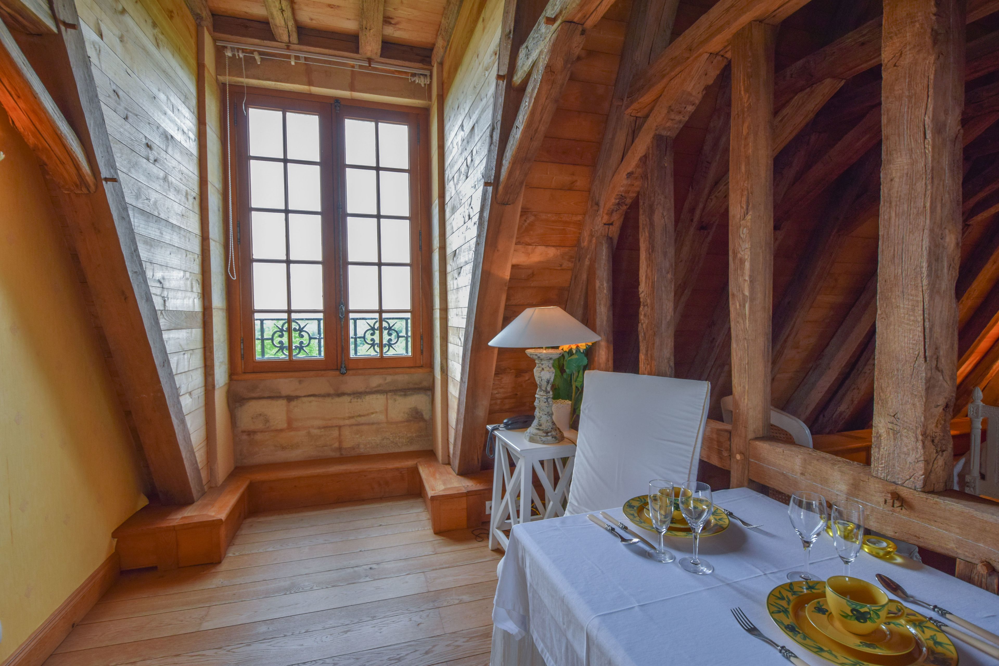 A dining area with a table set for two, a window with a view, and wooden beams on the ceiling.