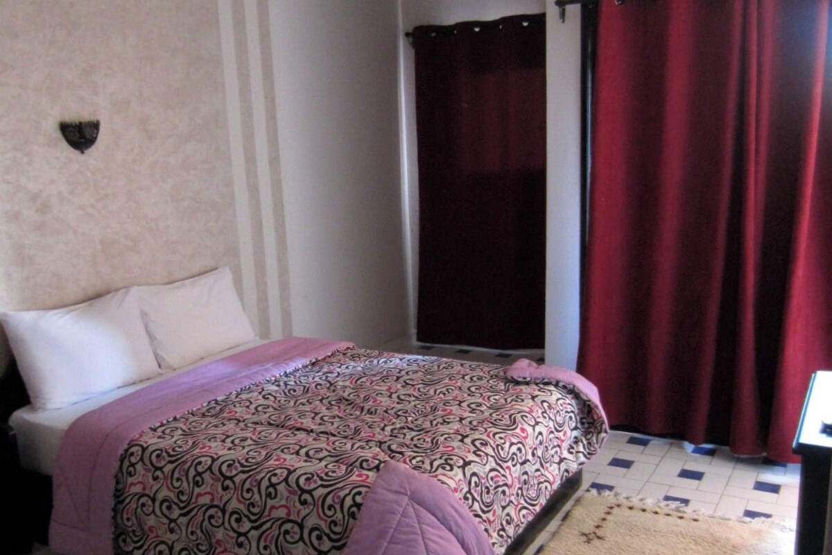 A bedroom with a bed, a ceiling fan, a window with curtains, and a radiator.