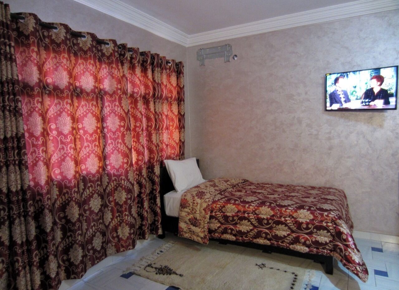 Un dormitorio con una cama, cortinas, un televisor y una lámpara fijada a la pared.