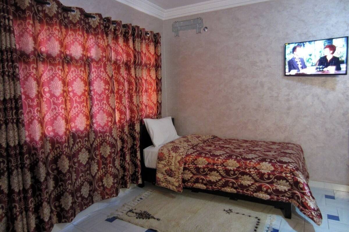 Un dormitorio con una cama, cortinas, un televisor y una lámpara fijada a la pared.