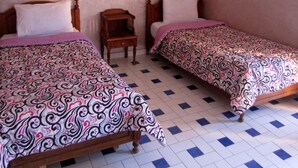 Una habitación con dos camas de madera, una mesita de noche pequeña de madera, una lámpara de pared y un ventilador de techo.