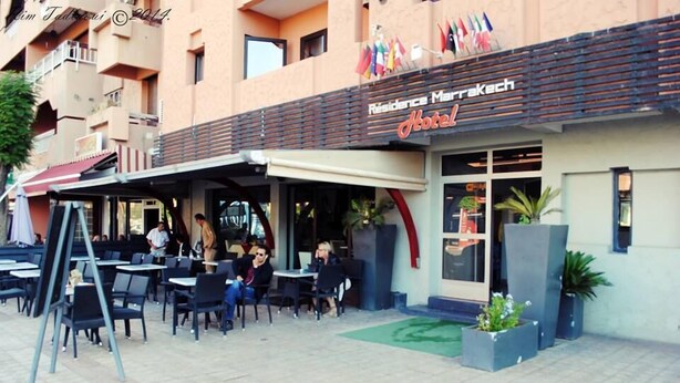 Exterior de un hotel con asientos exteriores, un patio cubierto y un cartel que dice