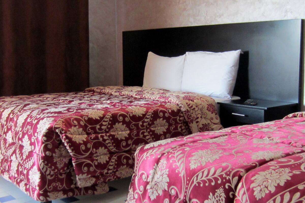 Habitación de hotel con dos camas, cada una con una colcha estampada, una mesita de noche negra y un almohadón blanco.