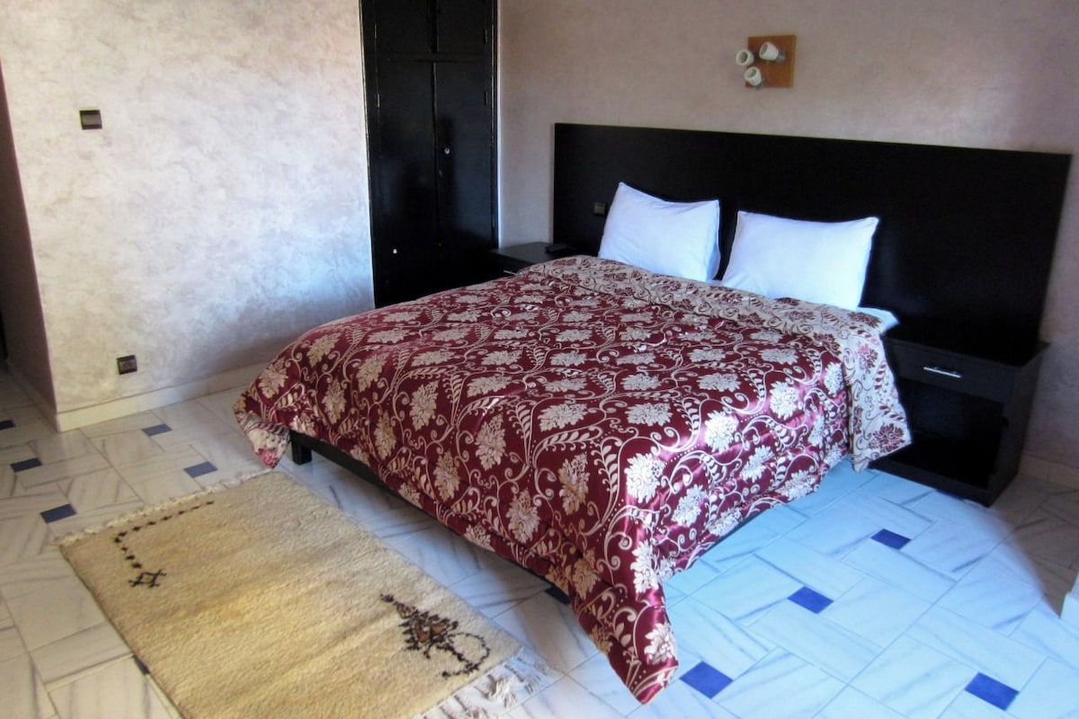 Un dormitorio con cama, mesita de noche, lámpara de pared y puerta.