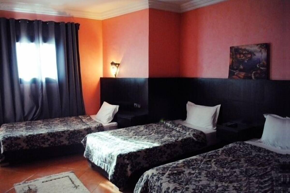 Una habitación de hotel con dos camas, una mesita de noche, una lámpara y un cuadro en la pared.
