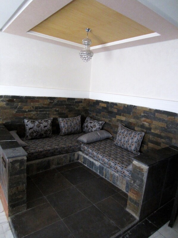 A corner seating area with a stone wall and a ceiling fan. - Hotel Marrakech Residence (Marrakech)