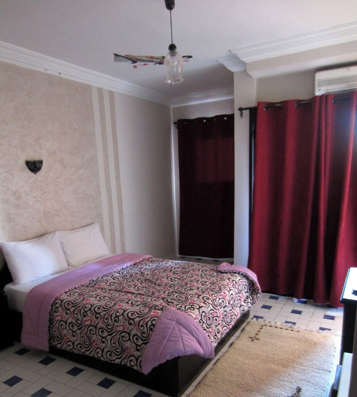 Un dormitorio con cama, ventilador de techo, ventana con cortinas y radiador.