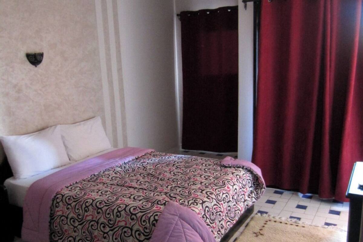 Un dormitorio con cama, ventilador de techo, ventana con cortinas y radiador.