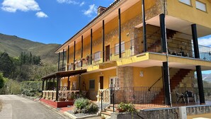 A yellow multi-story building with balconies, a covered porch, and a mountain backdrop. - Spa Rural Mirador de Miranda (Belmonte de Miranda)