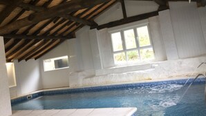 An indoor swimming pool with a tiled edge, a wooden ceiling, and a window with a view of greenery. - Spa Rural Mirador de Miranda (Belmonte de Miranda)