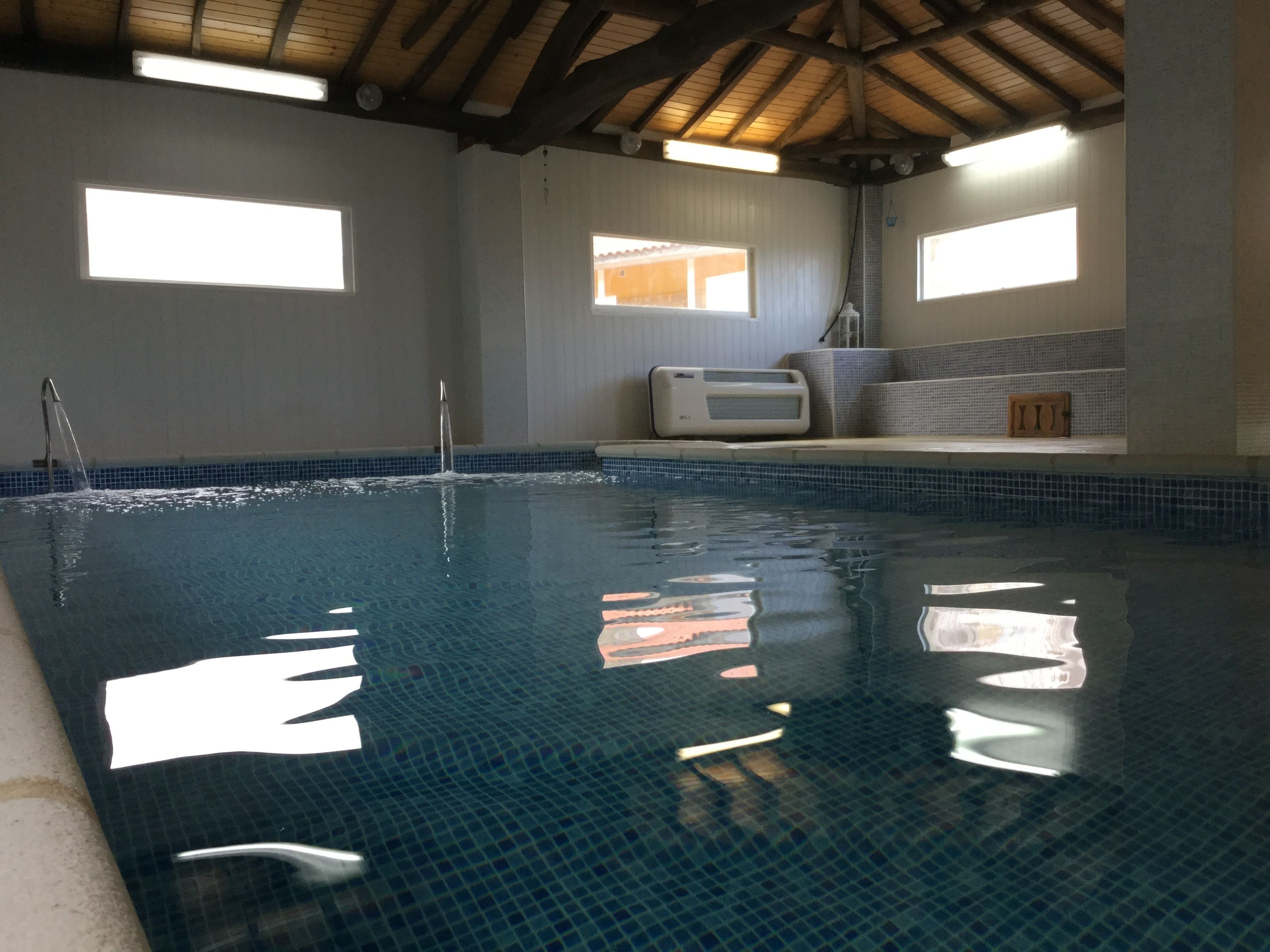 Una piscina con agua azul cristalina, techo de madera y paredes con azulejos.