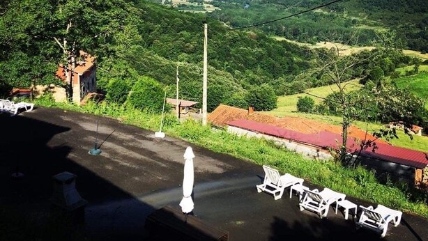 A view of a mountainous landscape with a rainbow, a paved area with white chairs, and a small building with a red roof. - Spa Rural Mirador de Miranda (Belmonte de Miranda)