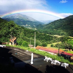 A view of a mountainous landscape with a rainbow, a paved area with white chairs, and a small building with a red roof. - Spa Rural Mirador de Miranda (Belmonte de Miranda)