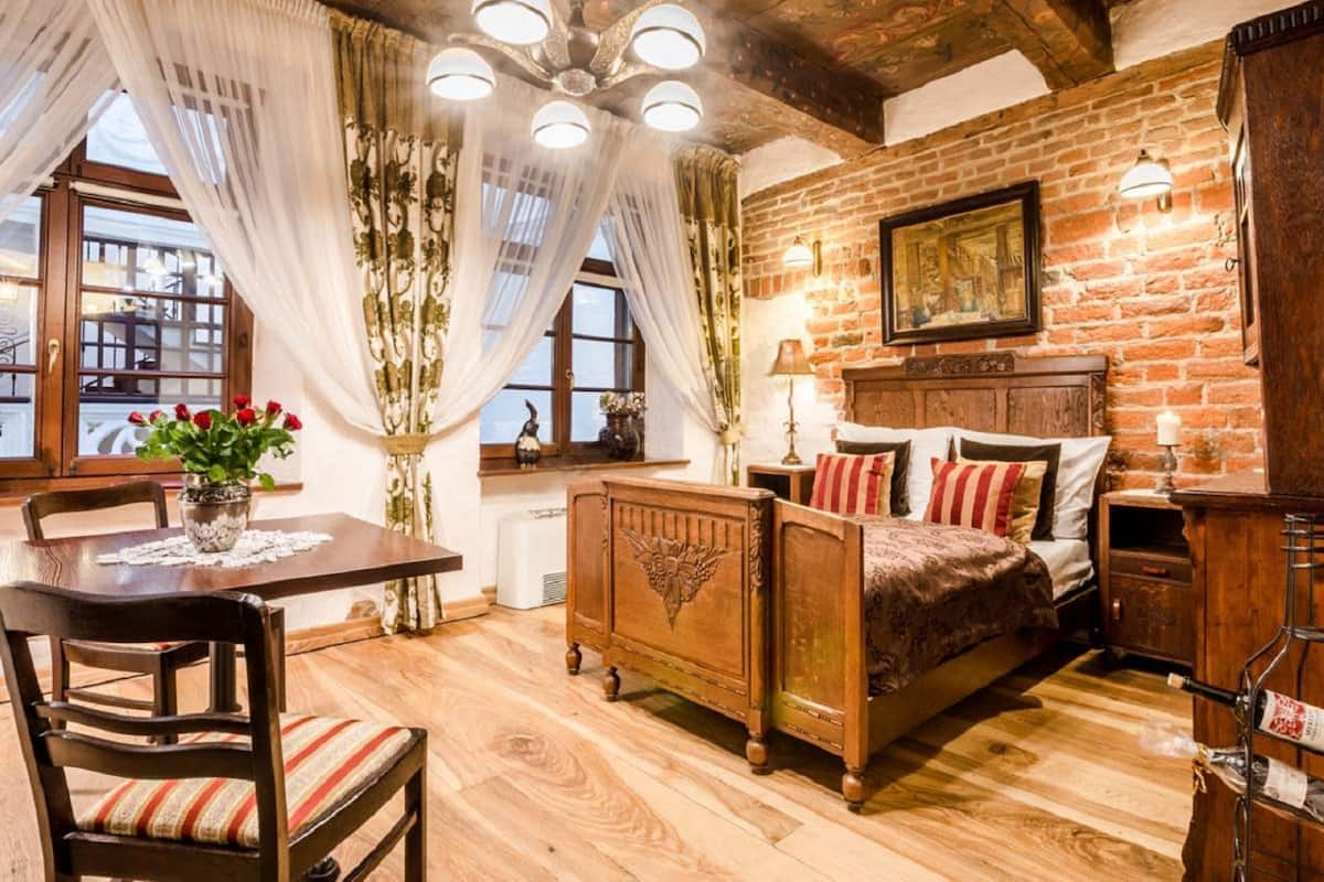 A rustic bedroom with a wooden bed, a dining table with chairs, and a chandelier.