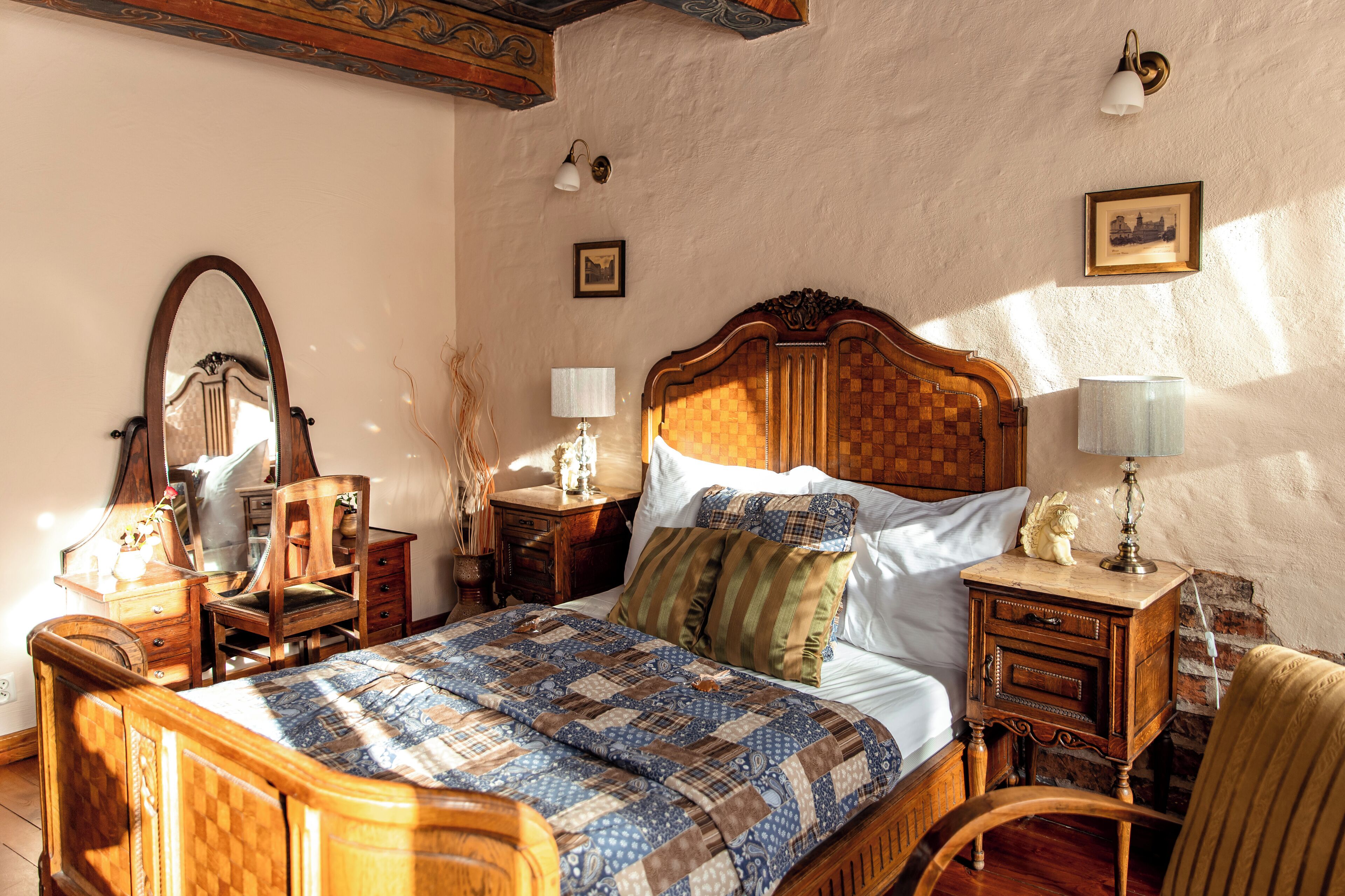 Ein traditionell eingerichtetes Schlafzimmer mit einem hölzernen Bett, einem Nachttisch mit Lampe, einer Kommode und einem Spiegel.