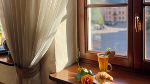 Udsigt til bygninger fra et vindue, et bord med et glas drik, en croissant og en rose.