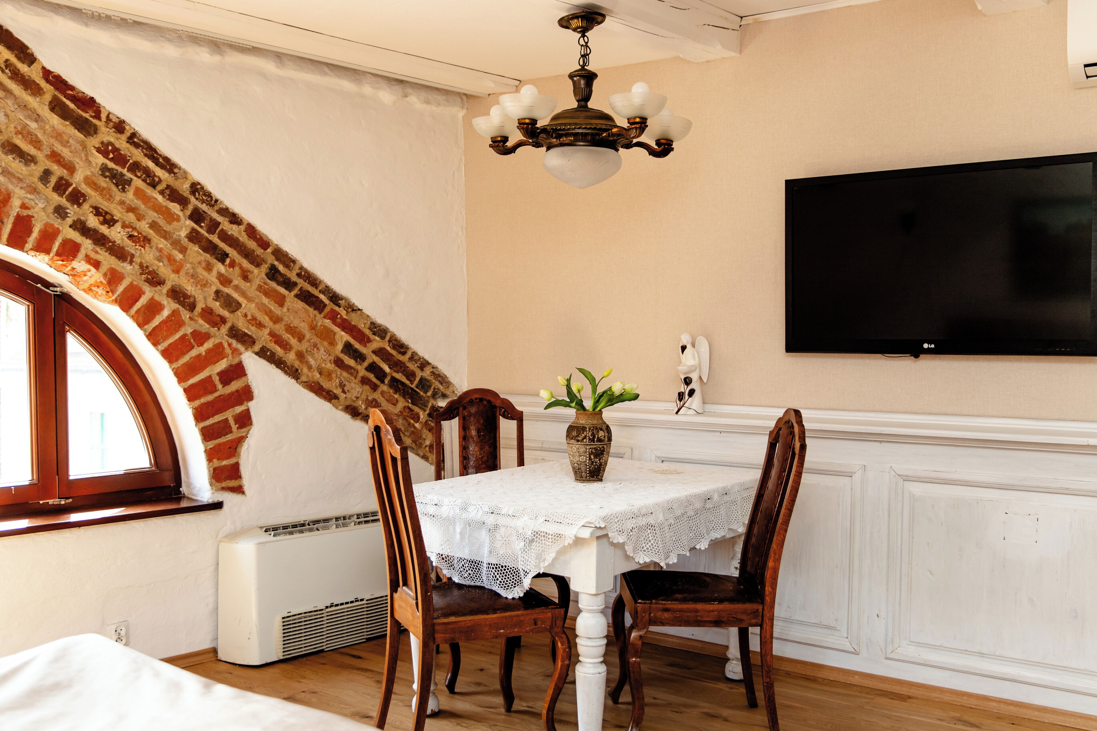 A dining area with a table, chairs, a chandelier, a television, and a brick wall.