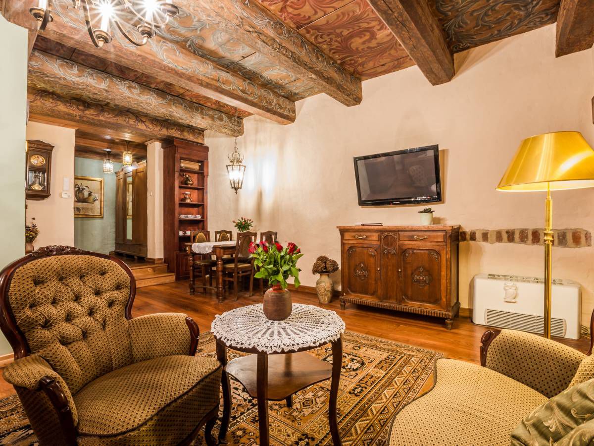 Una sala de estar acogedora con techo de madera, un televisor, una lámpara y un comedor con sillas y una mesa.