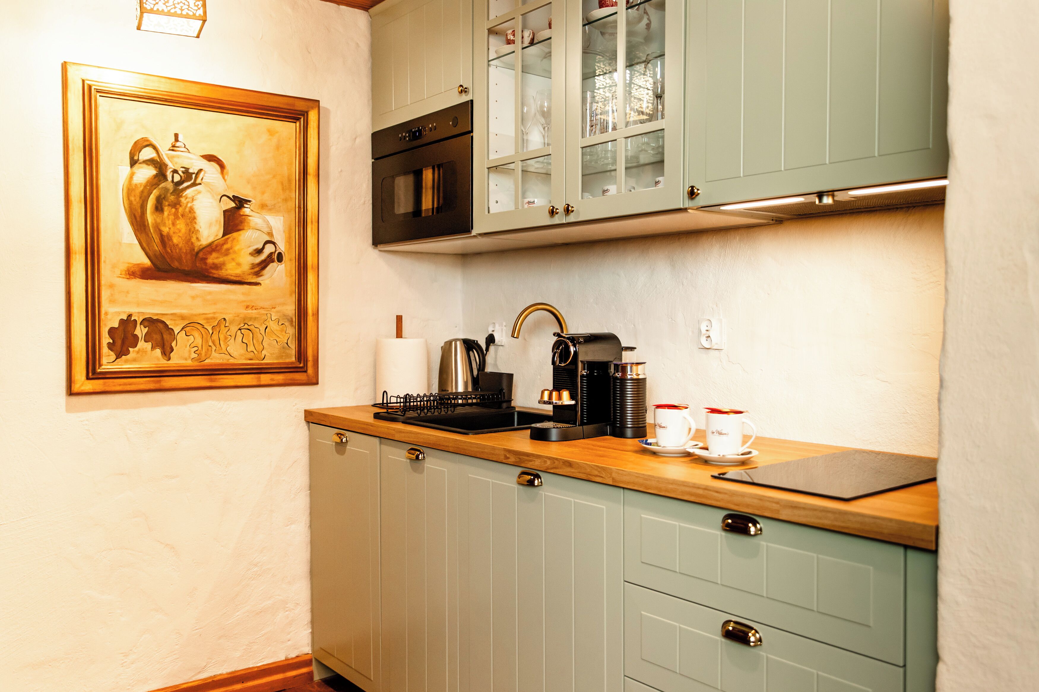 A kitchen with a wooden countertop, a coffee machine, and a framed painting on the wall.