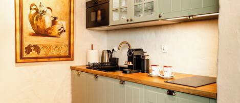 A kitchen with a wooden countertop, a coffee machine, and a framed painting on the wall.