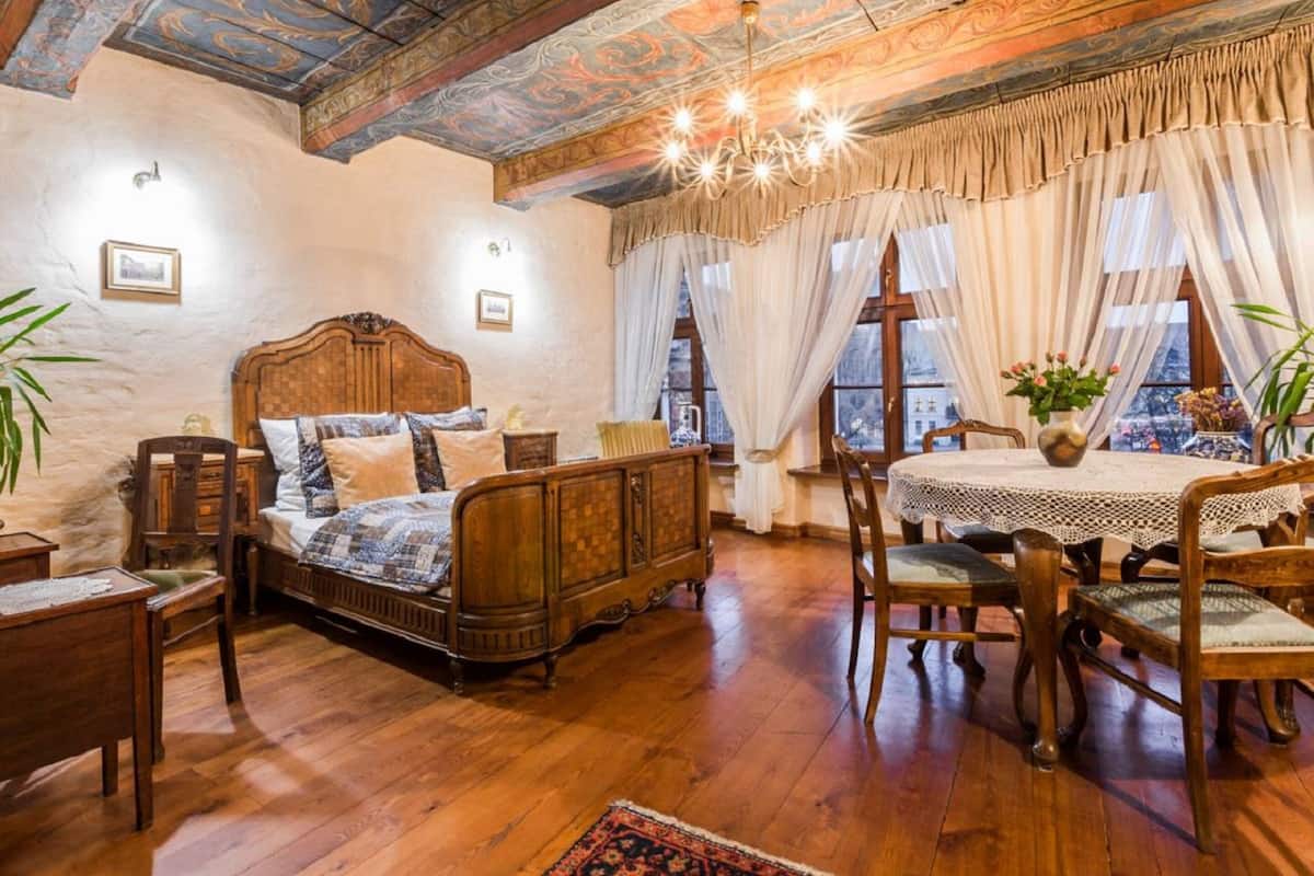 A traditional room with a wooden bed, a dining table with chairs, and a view of the city through large windows.