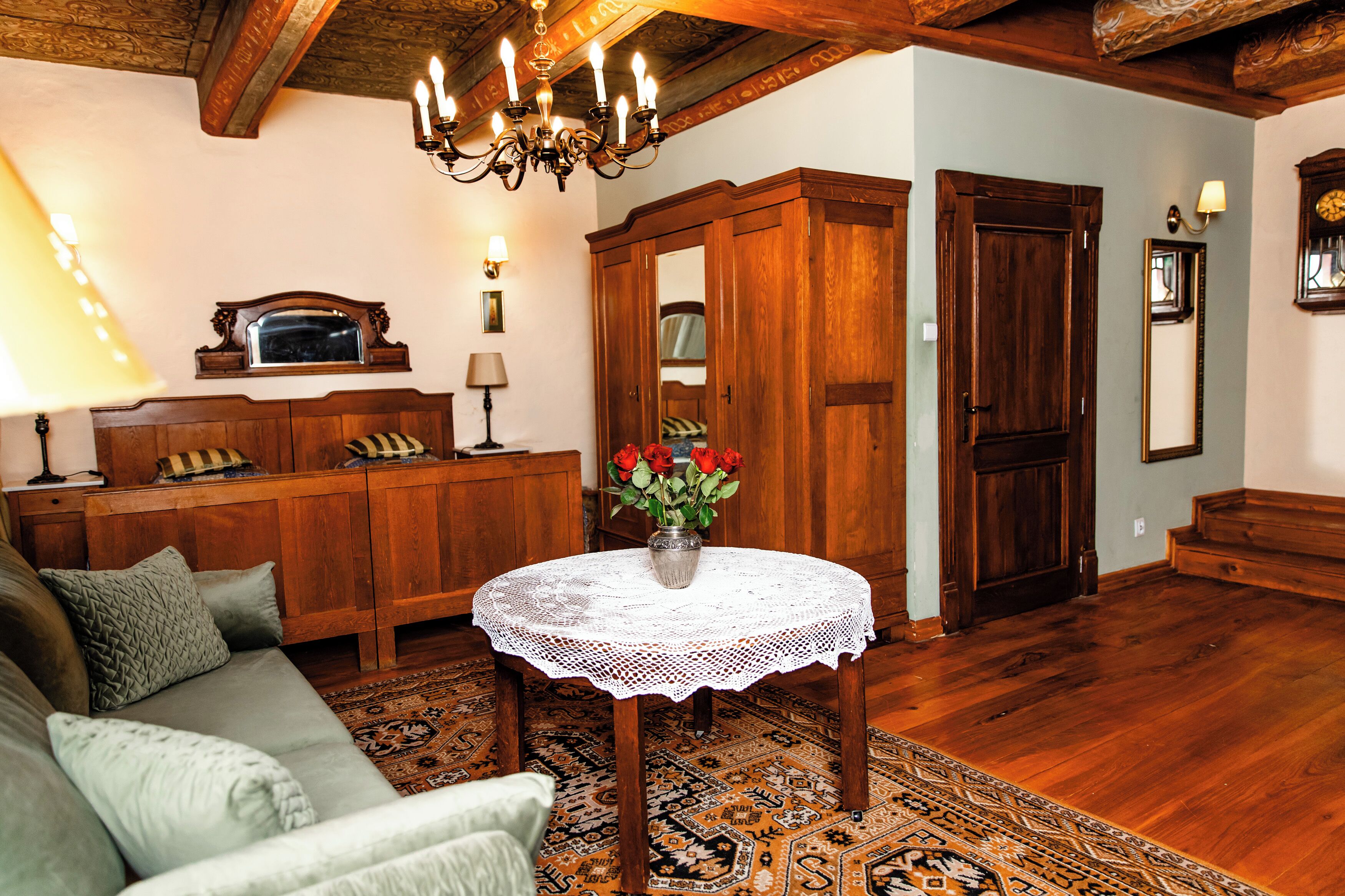 Una sala de estar acogedora con un sofá de madera, una mesa redonda con mantel de encaje, un aparador de madera y una araña.