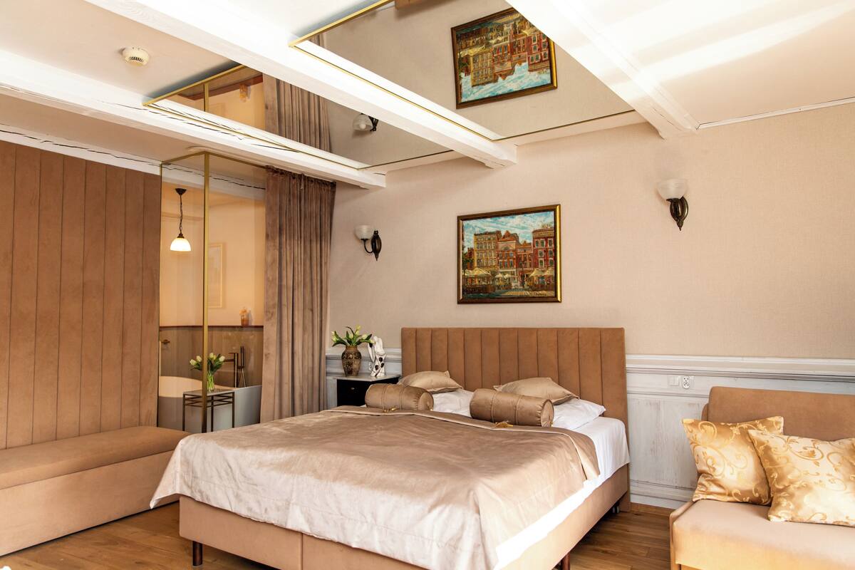 A modern hotel room with a large bed, a sofa, a small table with a vase, and a painting on the wall.