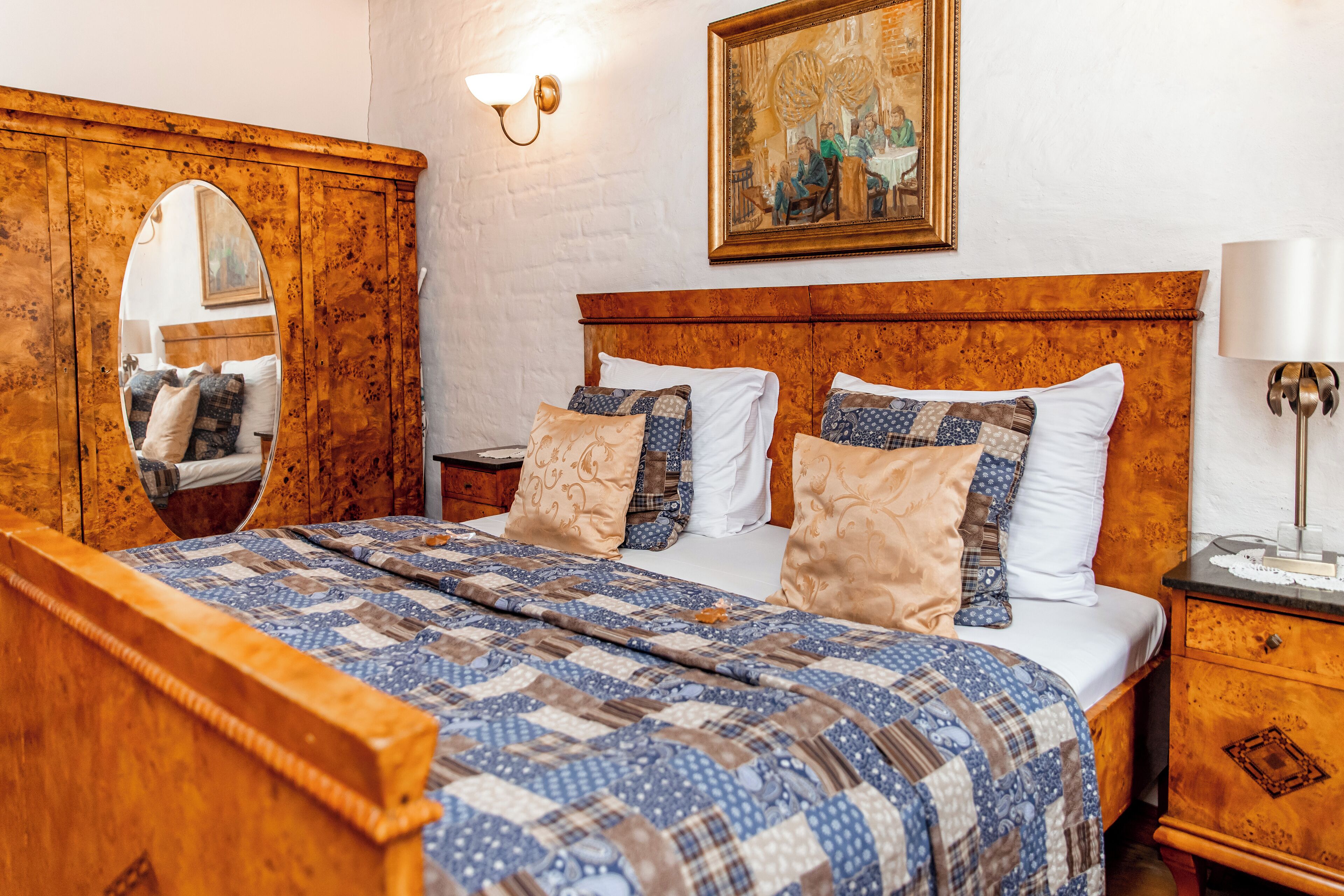 A neatly made bed with a quilt, a wooden headboard, a nightstand with a lamp, and a painting on the wall.