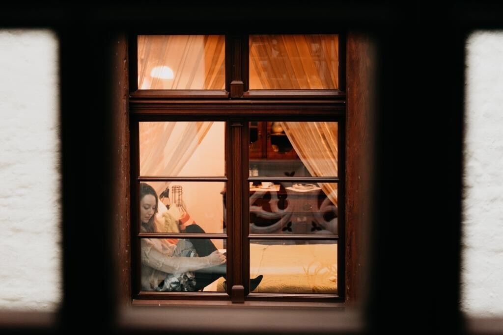 Una ventana con marco de madera y vistas a una habitación con una cama y una persona sentada.