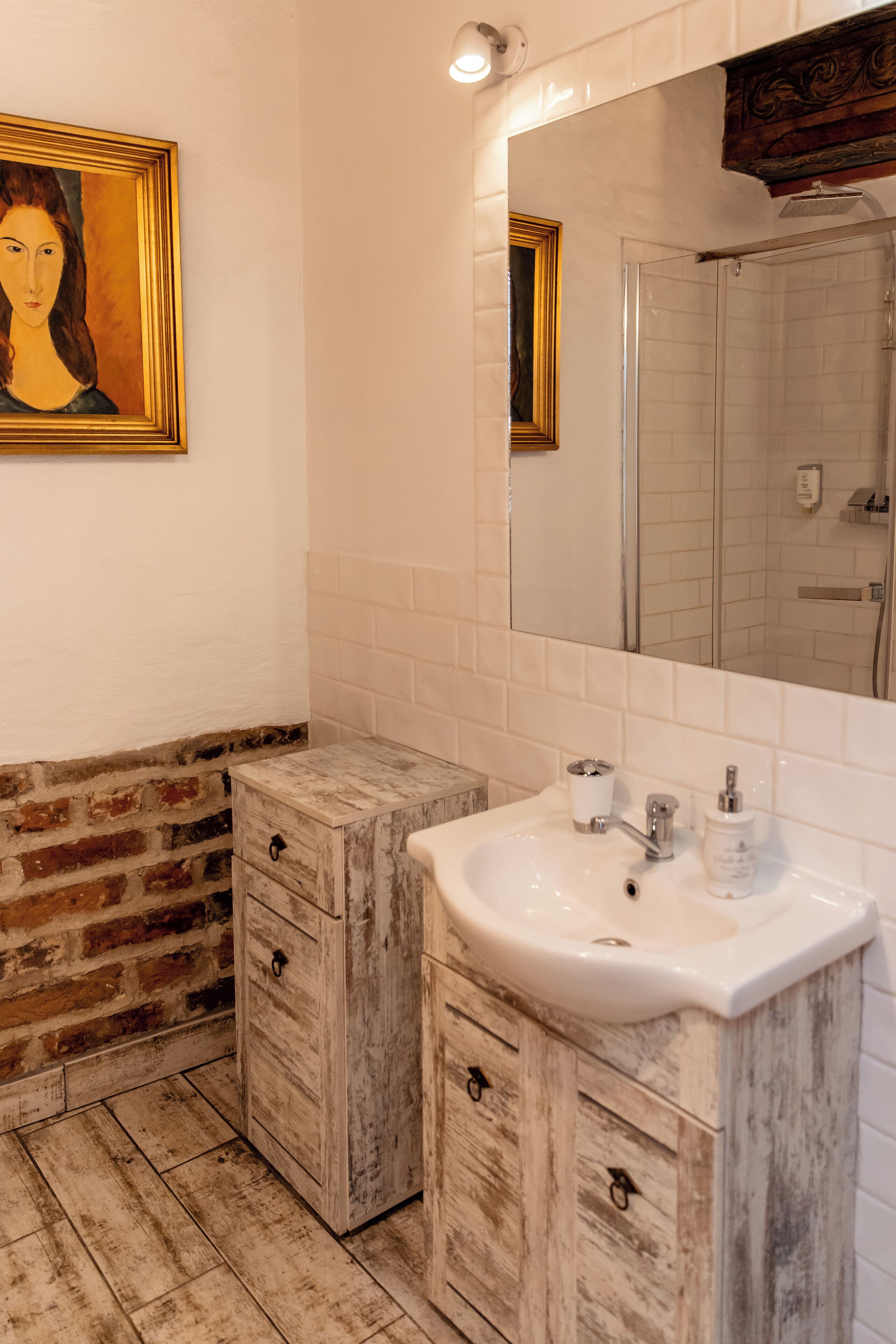 A bathroom with a white sink, wooden cabinets, a mirror, and a framed painting on the wall.