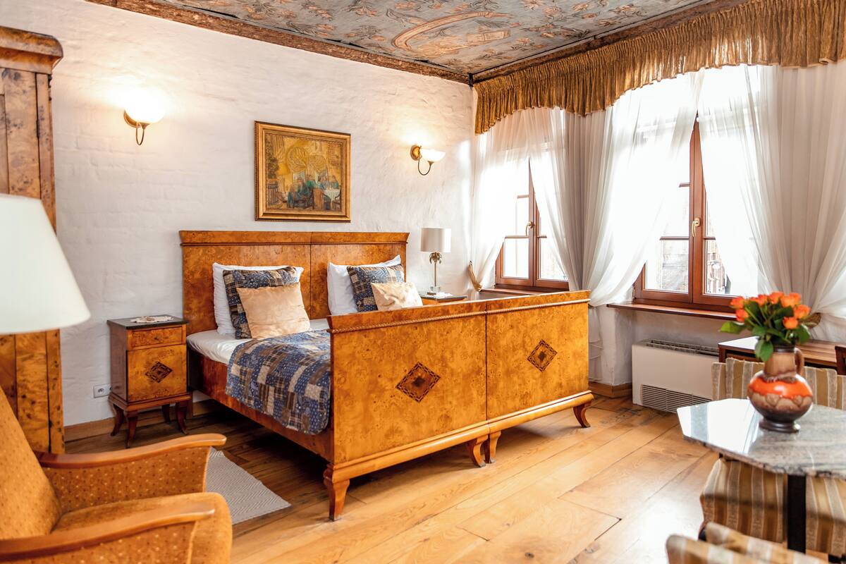 A traditional bedroom with a wooden bed, a nightstand, a chair, and a table with a vase.