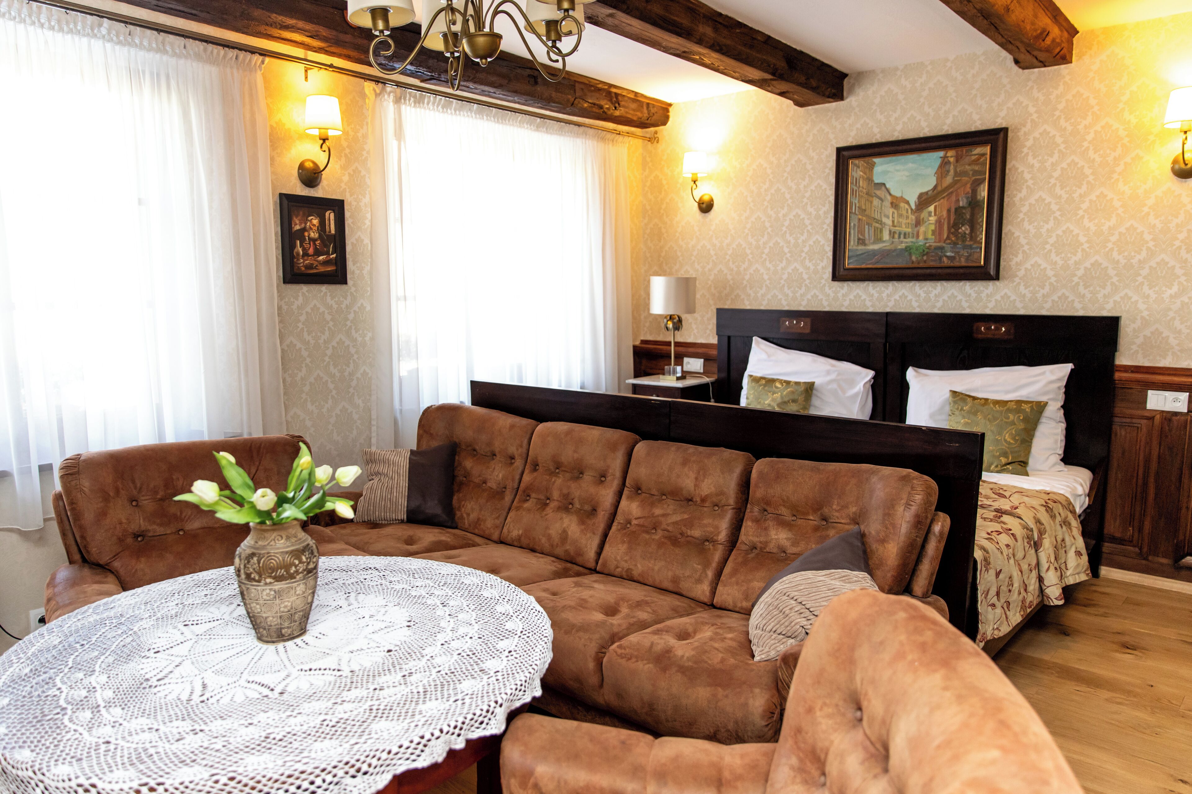 Una habitación acogedora con un sofá marrón, una mesa redonda con un jarrón, una cama con almohadas y un cuadro en la pared.