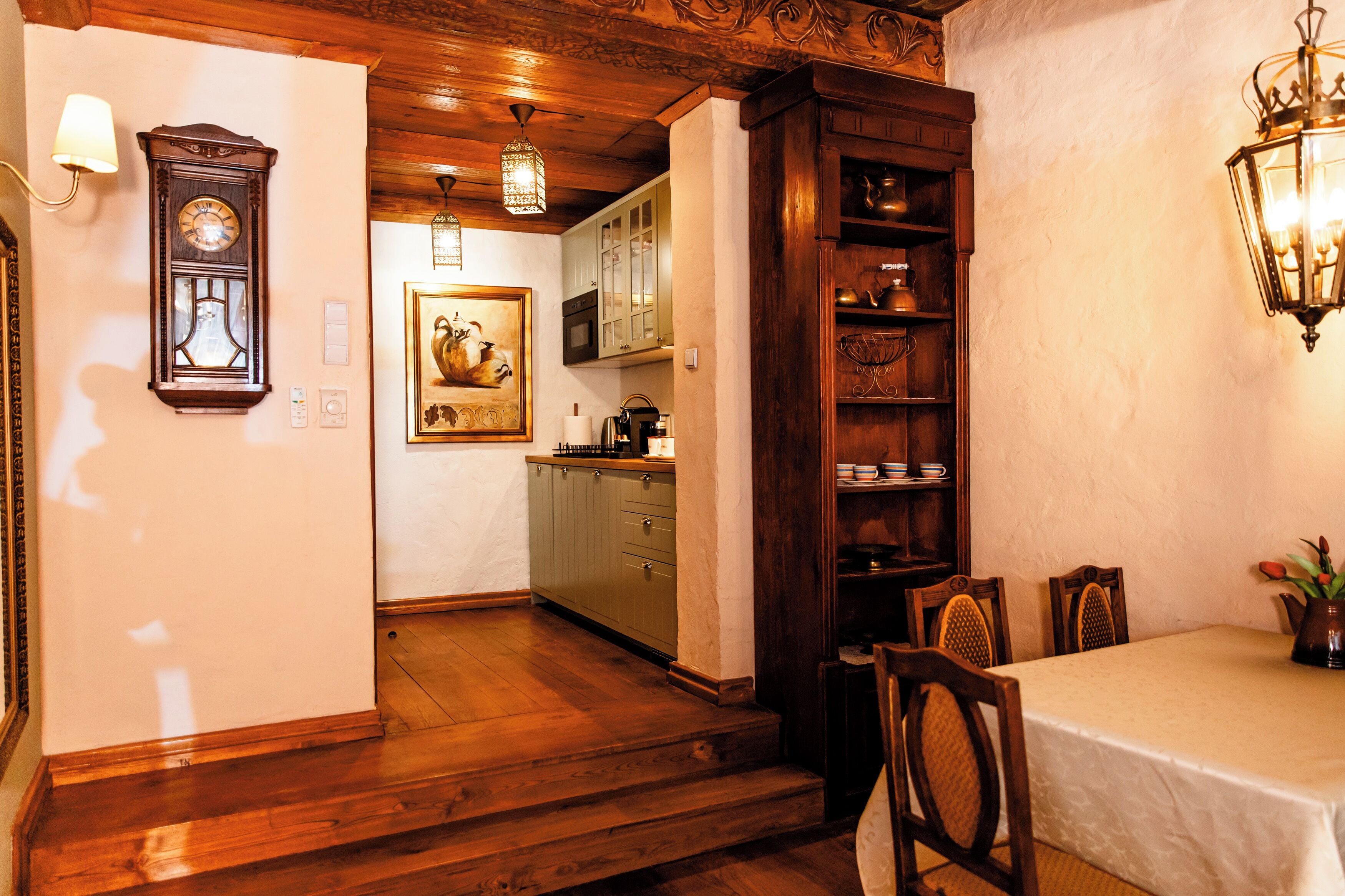 Eine Holztreppe führt zu einem Essbereich mit Tisch und Stühlen, eine Uhr an der Wand und eine Küche im Hintergrund.