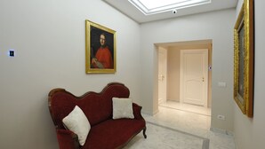 A hallway with a red velvet sofa, a painting on the wall, and a door at the end. - Angel Spagna Suite (Rome)