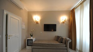 A room with a sofa, a TV mounted on the wall, and two wall sconces. - Angel Spagna Suite (Rome)