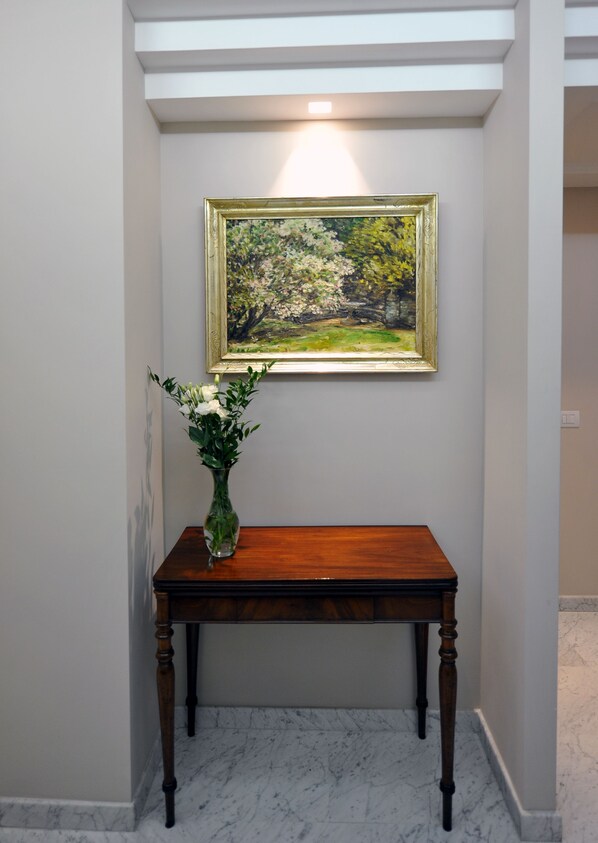 A marble-floored hallway with a wooden console table and a framed painting above it. - Angel Spagna Suite (Rome)